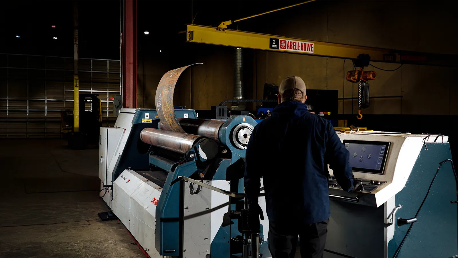 An American Wheatley fabricator operates a machine that bends sheet metal into a cylinder for HVAC equipment.