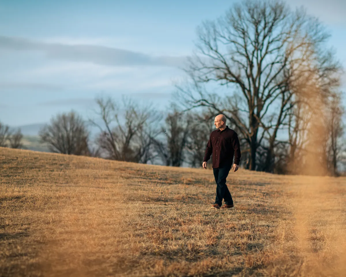 Brian Sanchez walks through an open field during his All Roads Lead Home cover shoot for Tulsa Real Producers.