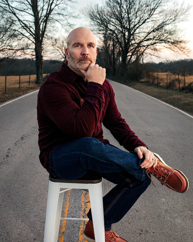 Brian Sanchez sits on a stool in the middle of a rural road during his All Roads Lead Home editorial shoot.