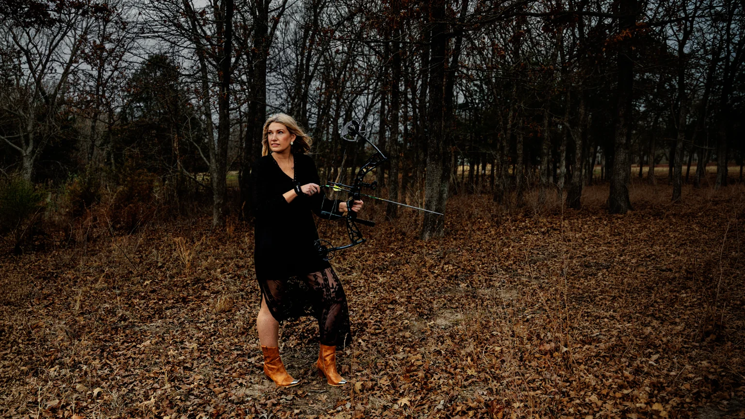 Cynthia Dixon holding a bow in a wooded setting during a Tulsa Real Producers editorial session.