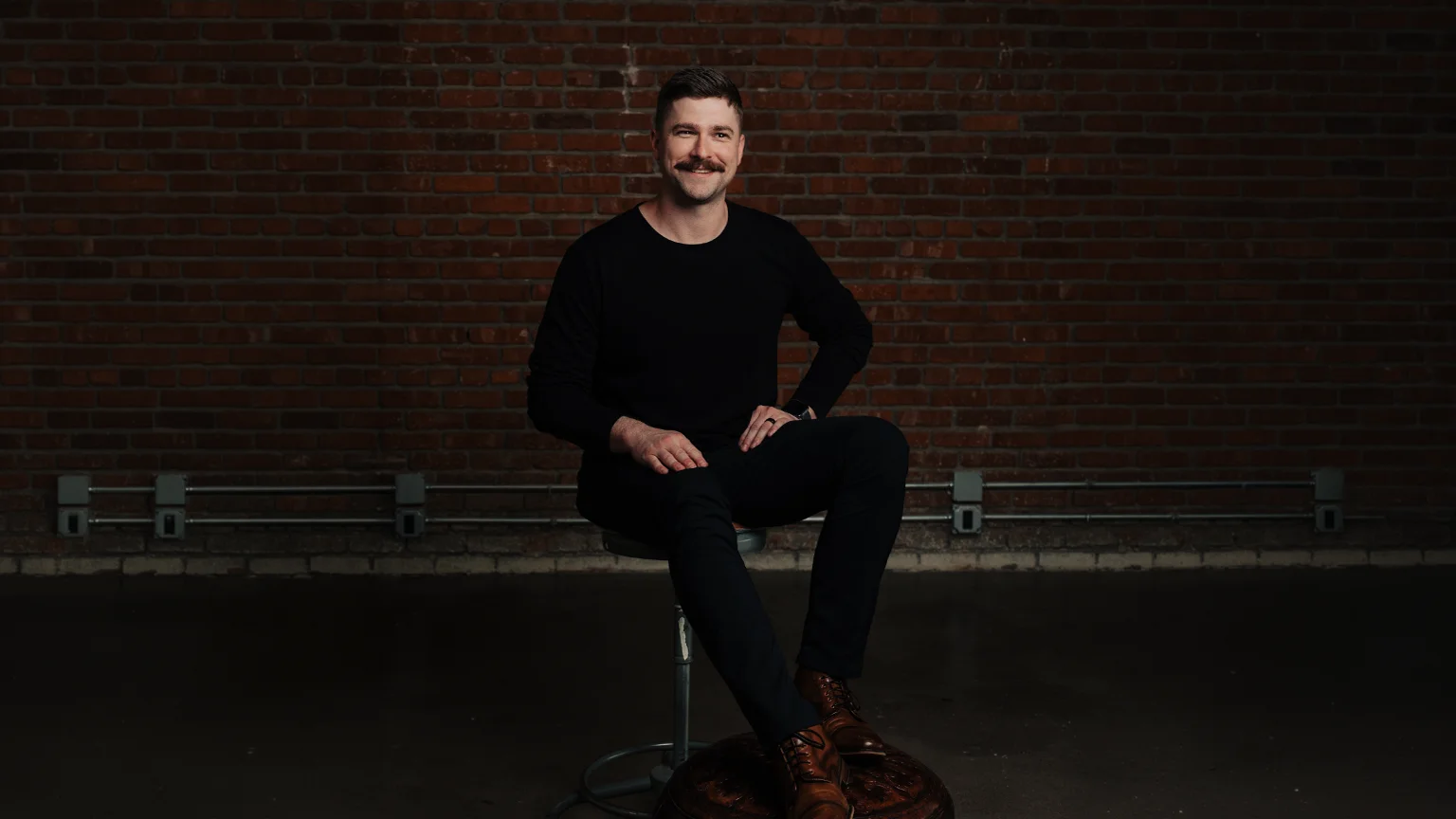 Darien Gibson, creative director and co-founder of WestSky Studio, seated against a brick wall in Tulsa.